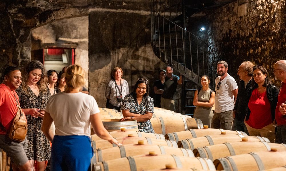 Eine Gruppe von Touristen besichtigt einen Weinkeller in Bordeaux und wird von einer Führerin an Weinfässern unterrichtet.