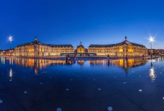 Nachtansicht des Place de la Bourse in Bordeaux mit beleuchteten historischen Gebäuden, die sich im Wasserspiegel widerspiegeln.