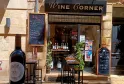 Ladenfront des Wine Corner, einer Weinbar in Bordeaux, mit ausgestellten Weinflaschen, Außenbereich mit hohen Tischen und Werbeplakaten.
