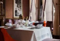 Eleganter Gourmet-Restaurantraum mit gedecktem Rundtisch, burgunderroten und orangefarbenen Polsterstühlen, feinem Glas, weißem Leinen und raffinierten Vorhängen im Pressoir d'Argent Gordon Ramsay in Bordeaux.