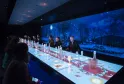 Futuristischer Speisesaal mit interaktivem leuchtendem Tisch, Panorama-Nachtansicht mit Mond und Bäumen auf Riesenbildschirm, Gäste auf beiden Seiten
