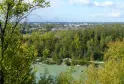 Panoramablick auf den Parc de l'Ermitage Sainte-Catherine in Bordeaux mit See im Vordergrund, Pappelwald und Stadtsilhouette unter bewölktem Himmel